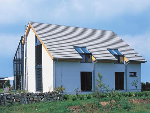 Moderne Doppelhaushälfte mit Satteldach und darunterliegenden Fenstern, umgeben von einem gepflegten Garten.