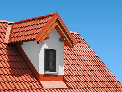 Dachansicht mit roter Ziegeldeckung und einem kleinen Fenster unter einem hellblauen Himmel.